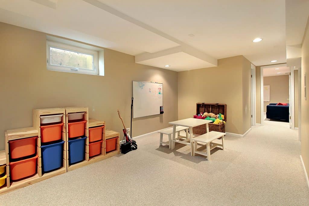 A cream painted basement wall with carpeted flooring and a small gaming table on the center