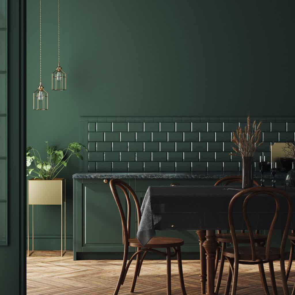A dark green themed dining area with a decorative green countertop and brick backsplash section, and wooden chairs