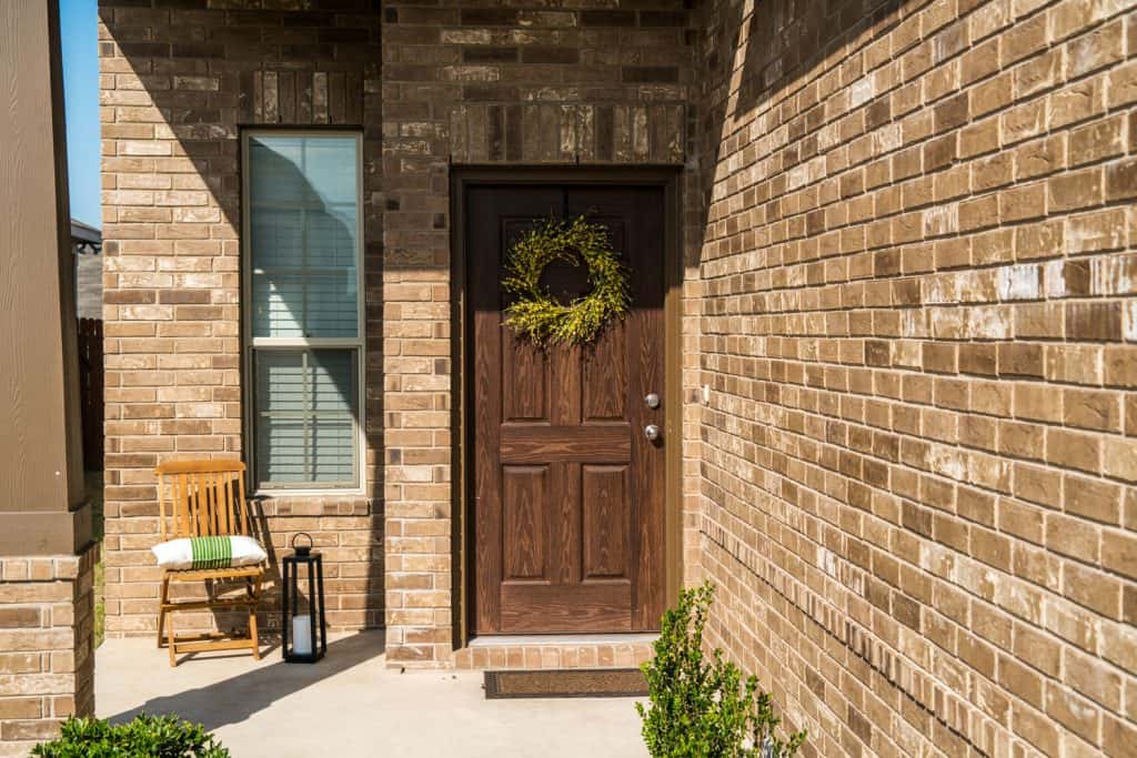 A decorative brick front porch with a hardwood front door with a wreath