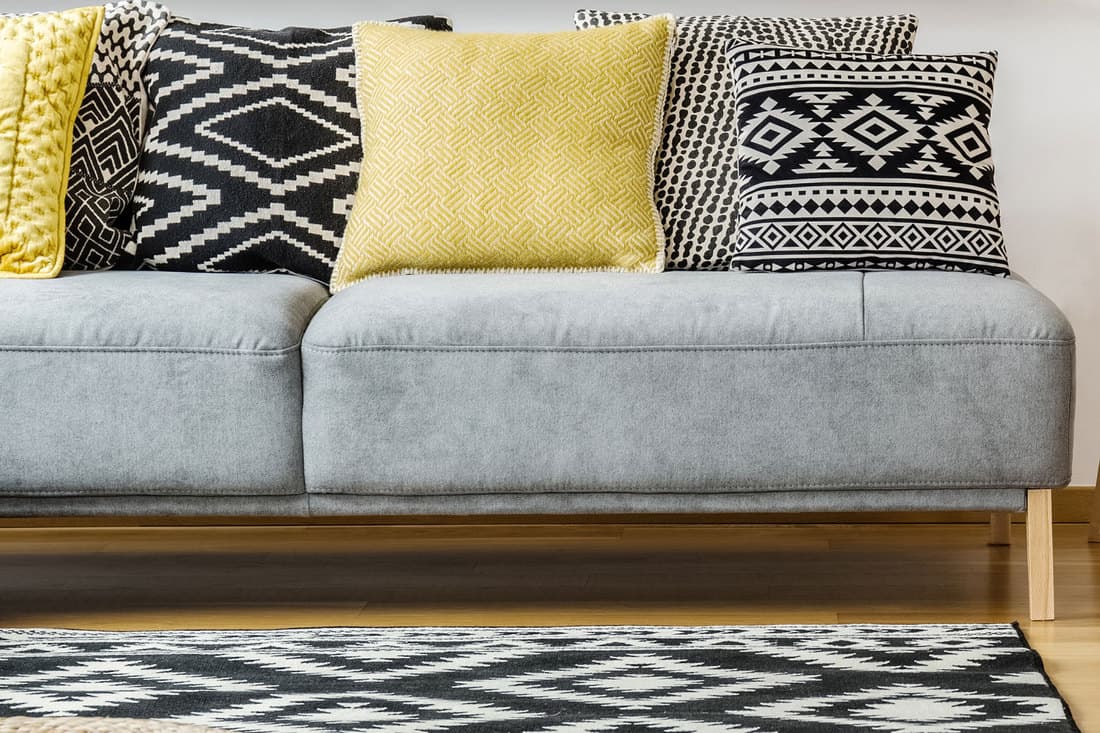 A detailed photo of a gray sofa with mustard yellow and black and white throw pillows