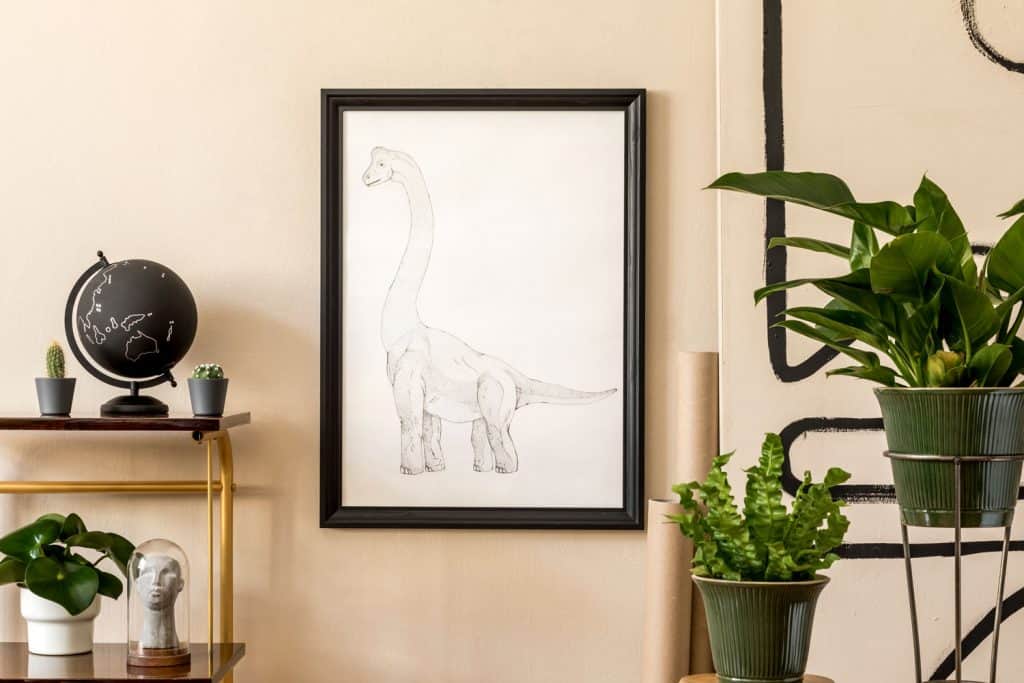 A dinosaur painting on the picture frame and indoor plants place on flower stands