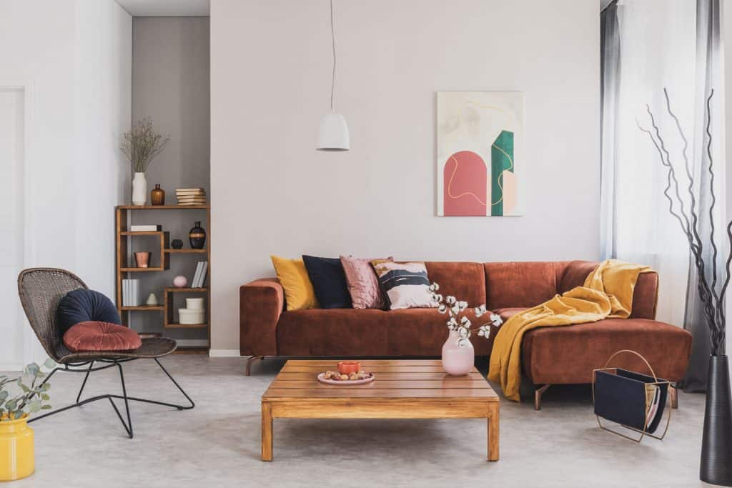 A gorgeous minimalist retro theme living room with a suede fabric sectional sofa, white painted walls with hanged painting, and a solid wooden coffee table