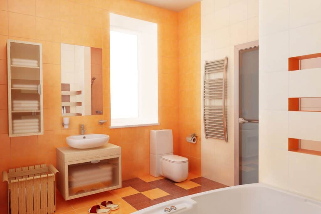 A gorgeous orange themed bathroom with and orange accent wall with a small vanity area and a white bathtub