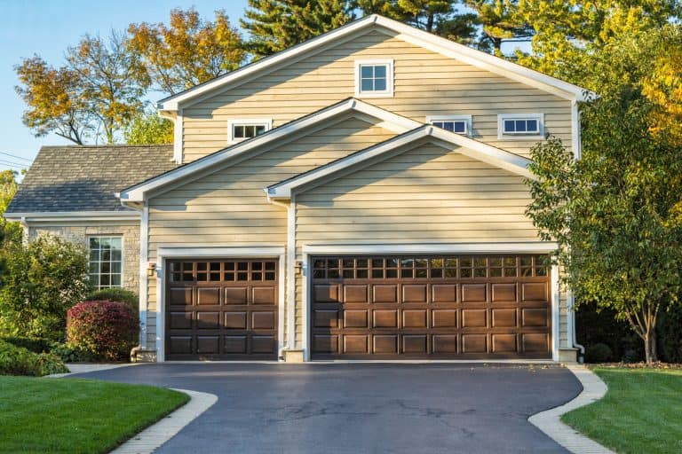 A gorgeous two storey house with cream colored wooden sidings, brown painted garage doors, and a white driveway, Can A Garage Door Be Wider Than The Opening?