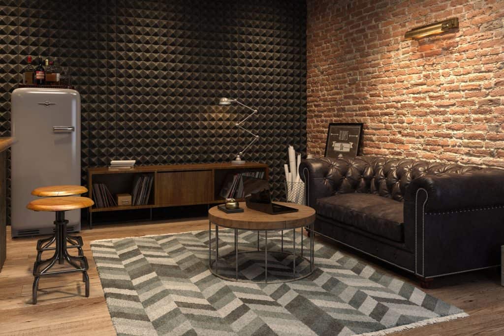 A gorgeous warm basement with brick decorative walls, black natuzzi sofa, and a solid round coffee table