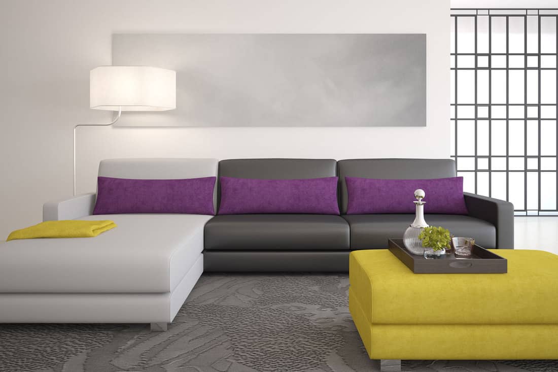 A gray and white sectional sofa with dark violet throw pillows and a mustard yellow ottoman