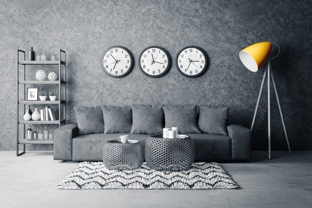A gray themed living room with a gray wallpaper with patterns, two coffee tables, and mustard colored floor lamp