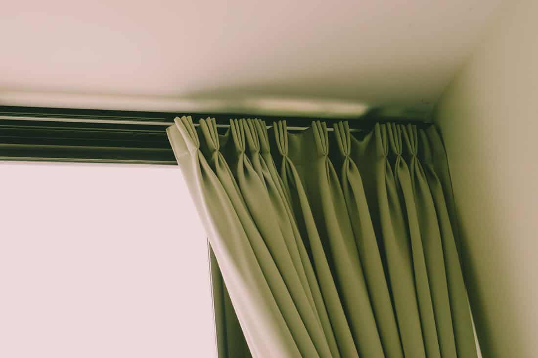 A green curtain hanged on the ceiling of a house, How To Hang Curtains From The Ceiling Without Drilling [6 Steps]