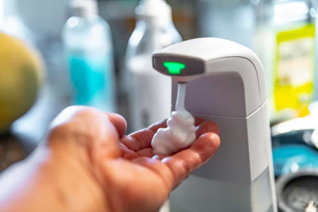 Une main posée sur un distributeur de savon automatique
