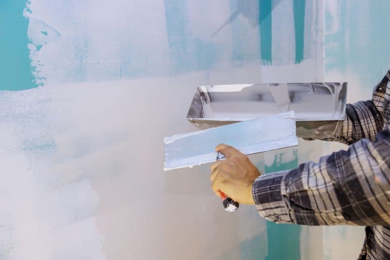 A hard working man putting spackle on the wall using plastering tools, How Long Does Spackle Take To Dry?