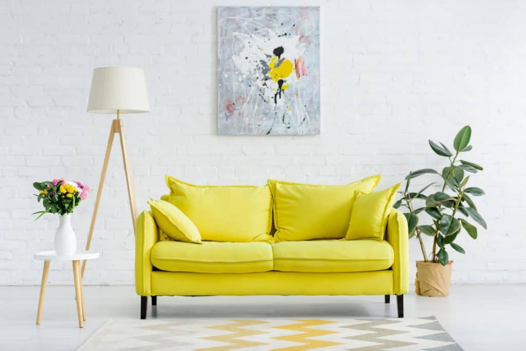 A light and elegant white colored living room incorporated with yellow loveseat sofa, indoor plants and a tripod floor lamp