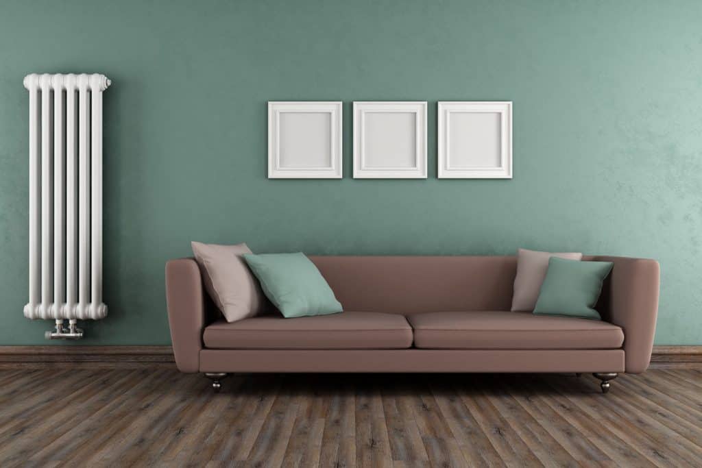 A light blue colored living room with a brown sofa with teal colored throw pillows, and a wooden flooring