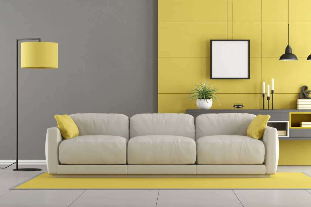 A light yellow colored living room with a light gray colored sofa, yellow carpet, and a tall yellow floor lamp