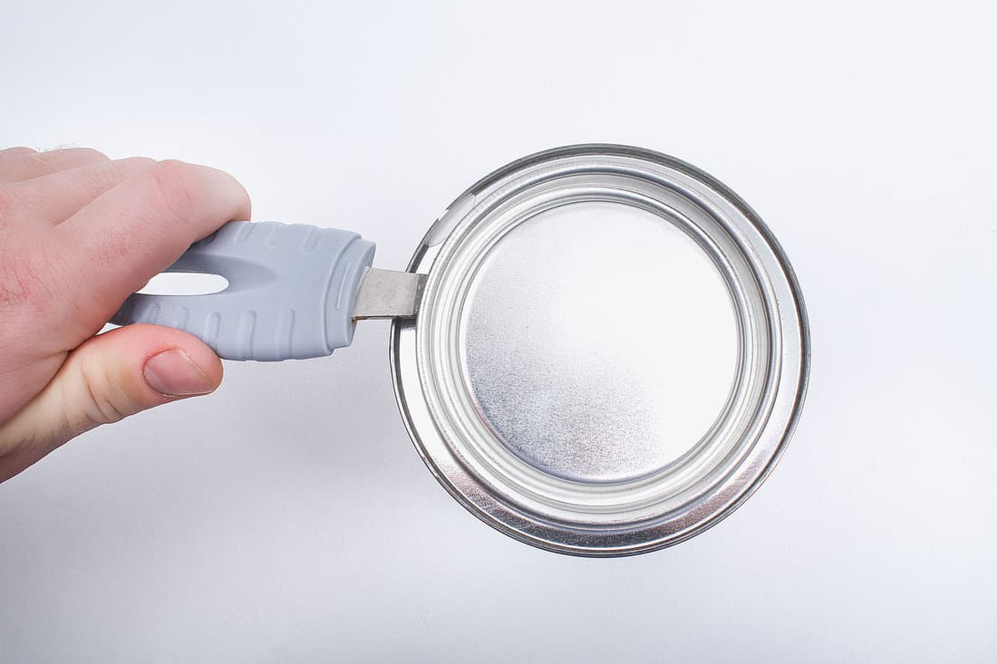A man opens a jar of white paint with a can opener on a white background. Renovation concept. 