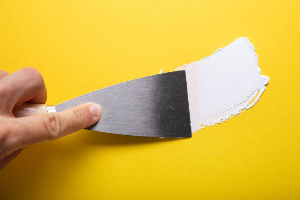 A man using a small plastering tool while applying spackle on a yellow wall with a crack