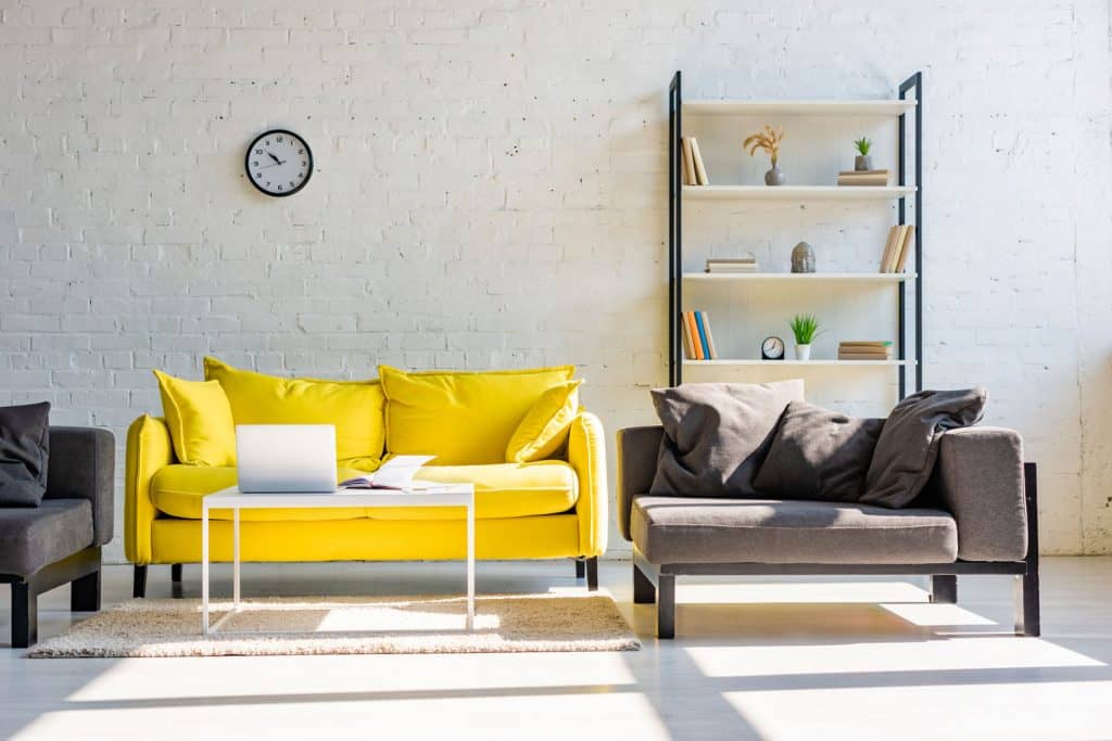 A minimalist industrial themed living room with a yellow sofa with yellow throw pillows mixed with gray sectional chairs