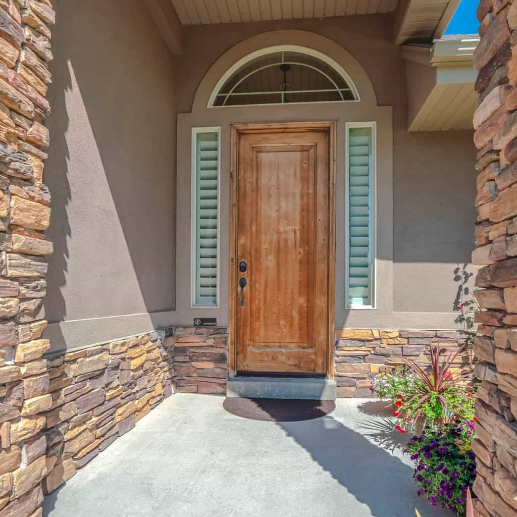 A modern front porch with decorative rock stone on the columns and a hardwood front door