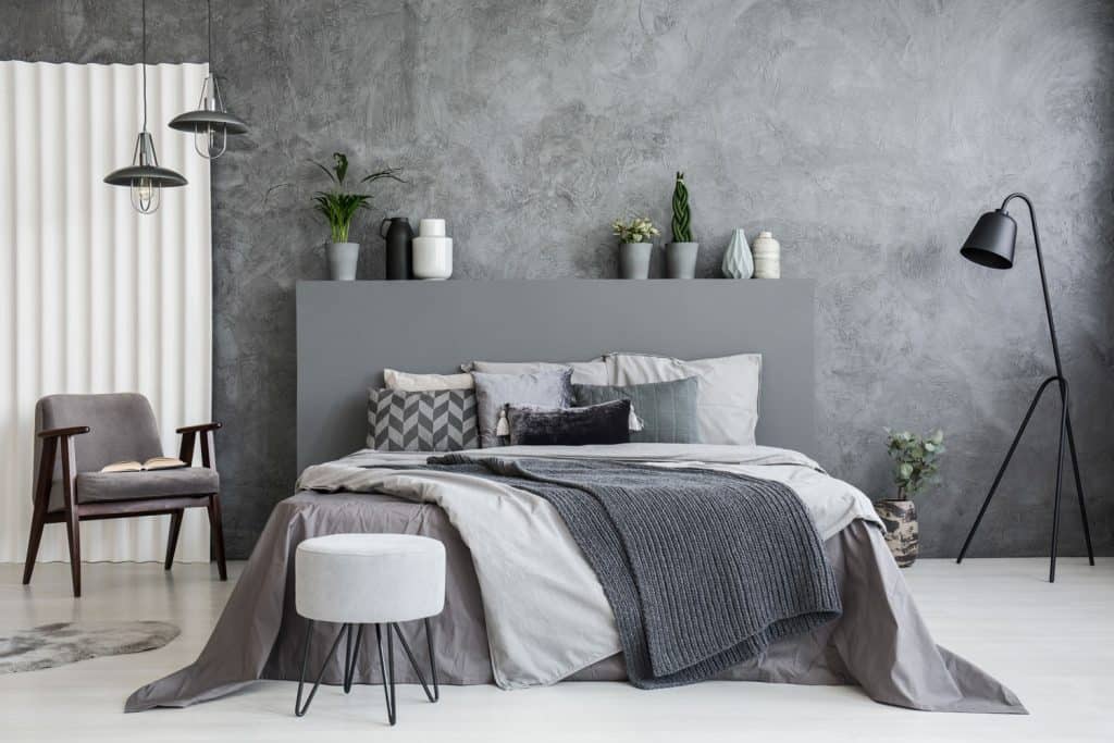 A modern gray themed bedroom with gray beddings, industrial floor lamps and ottoman, and indoor plants on top of the header