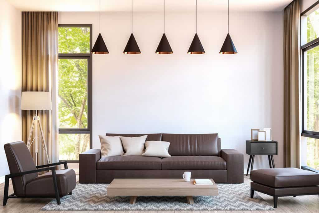 A modern luxurious living rom with white walls, black dangling lamps, brown leather sofas and ottoman
