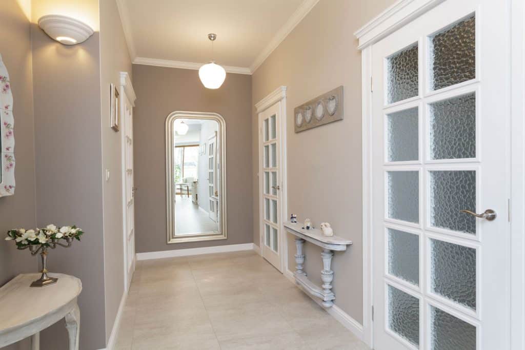 A narrow gray painted hallway with white painted doors panels and gray tiles