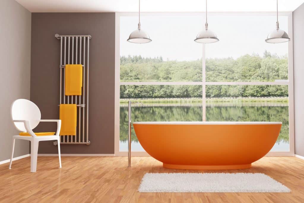 An orange colored bathtub inside a gray wall and wooden tiled bathroom with a huge picture window