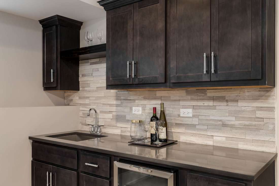 A residential wet bar with dark brown cabinets, granite counter tops, a sink, and wine refrigerator built-in.