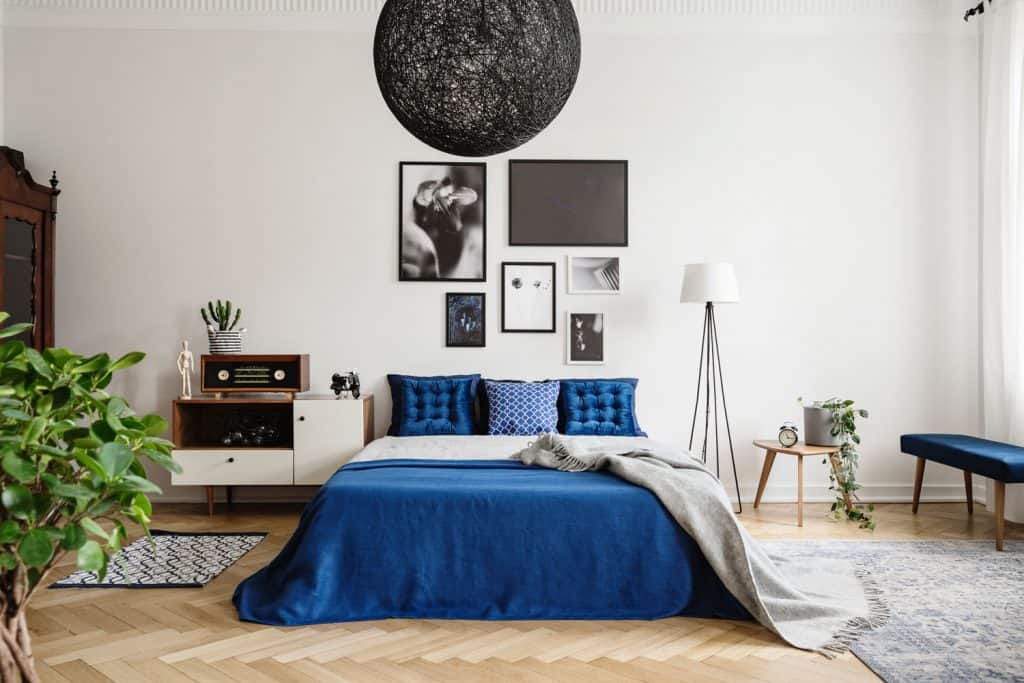 A retro themed living room with picture frames on the background, a bed with blue beddings, and a tripod design floor lamp