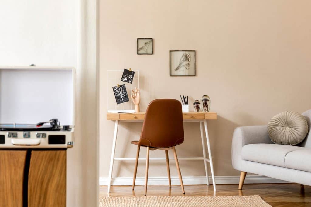 Un petit bureau à domicile minimaliste avec une petite table de bureau, des murs de couleur beige avec une chaise rouge et un canapé gris sur le côté