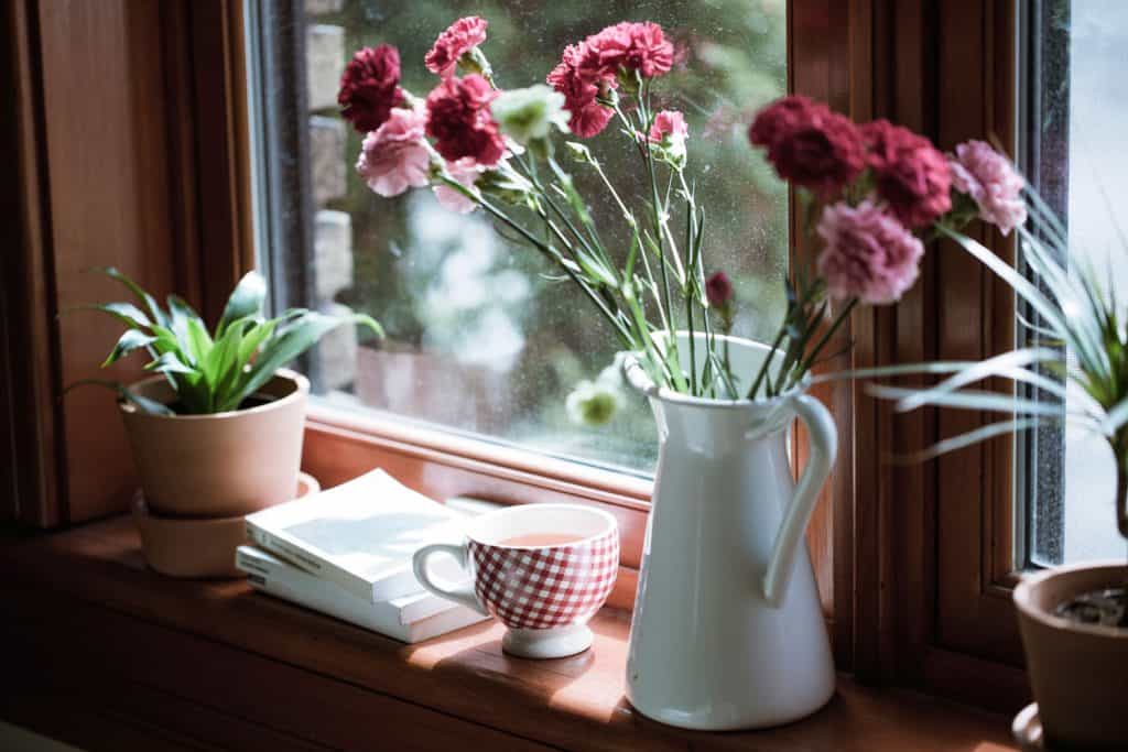 A small tea cup, books, and flowers on a vase placed on a wooden window