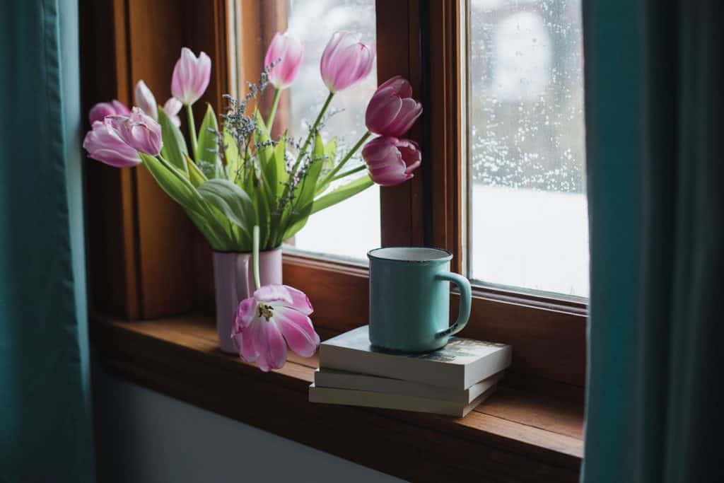 A small wooden framed window decorated with pink tulips and books
