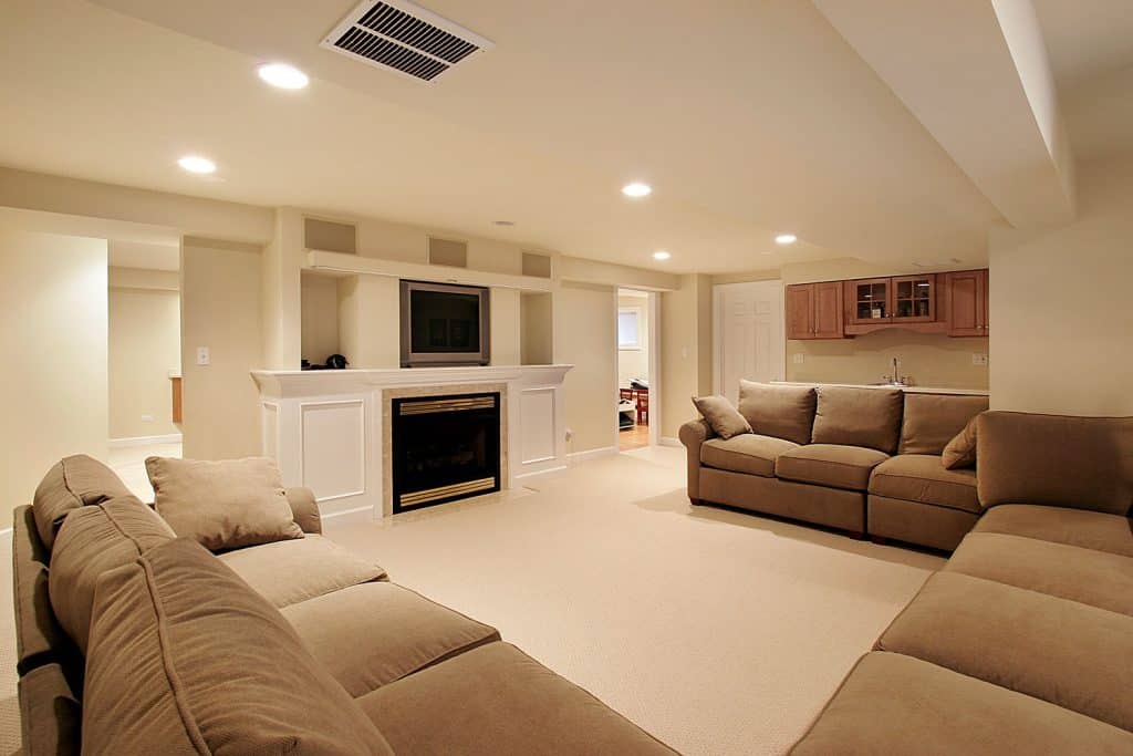 A spacious and comfortable basement floor with cream painted walls, brown cloth sofas, and a carpeted flooring