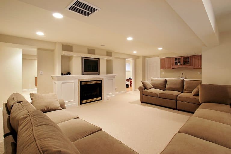 A spacious and comfortable basement floor with cream painted walls, brown cloth sofas, and a carpeted flooring, 17 Incredible Basement Interior Design Ideas