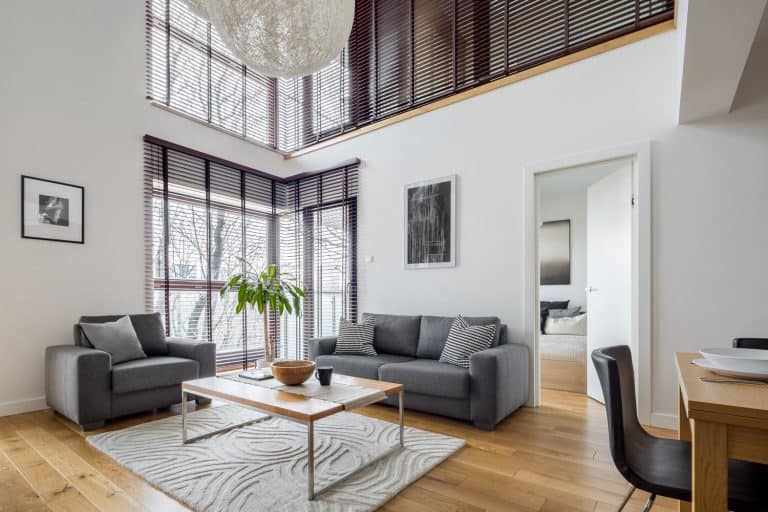 A two storey contemporary house with white walls, gray sofas, and a solid wooden coffee table, and a small are rug under it, 6 Colors That Make A Room Look Bigger And Brighter