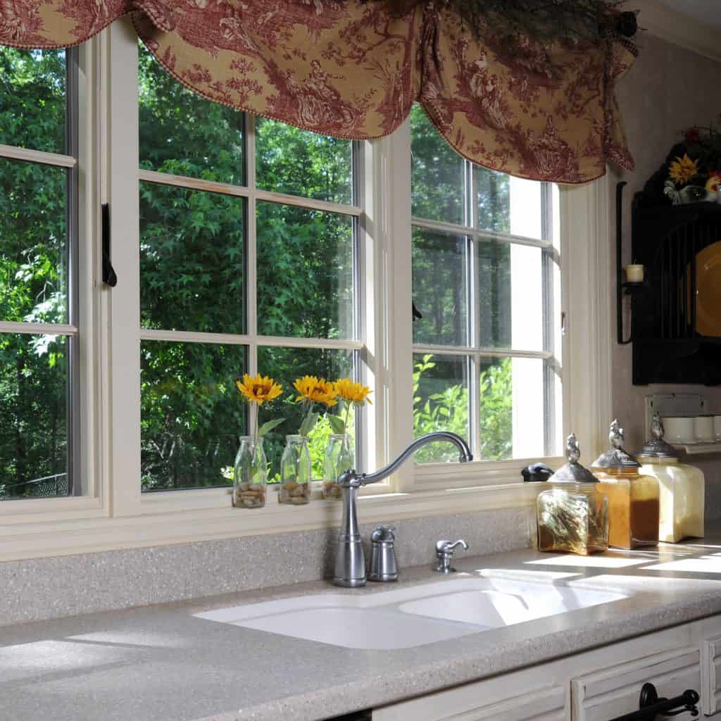 A vintage inspired kitchen area with a granite countertop, kitchen spices, and sunflowers on the window