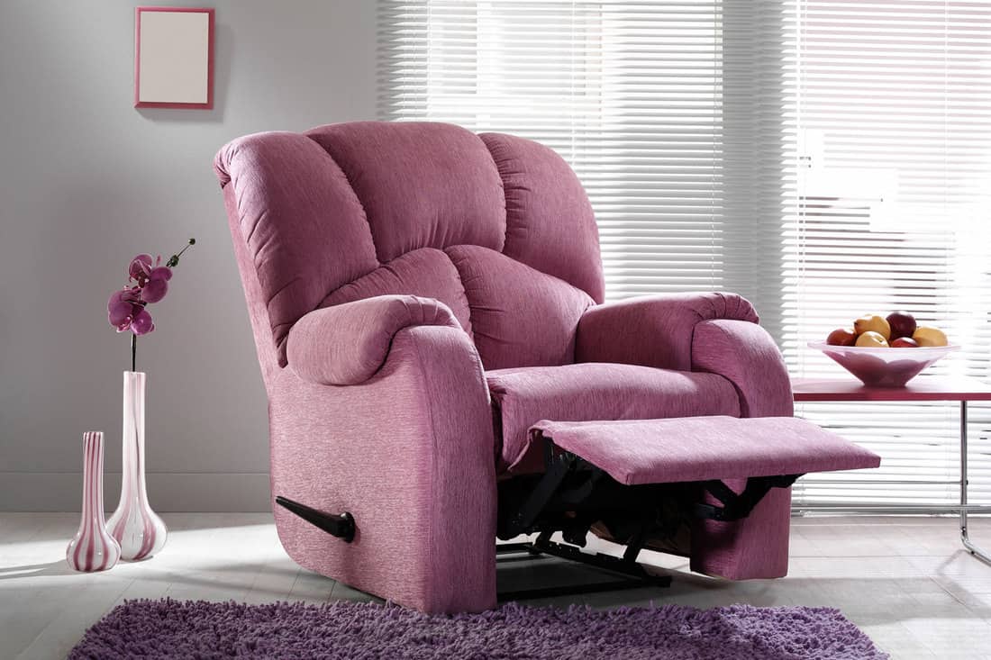 A violet reclining chair with a matching carpet on the floor inside a gray wall with blinds on the window, What Are The Most Comfortable Chairs For A Living Room?