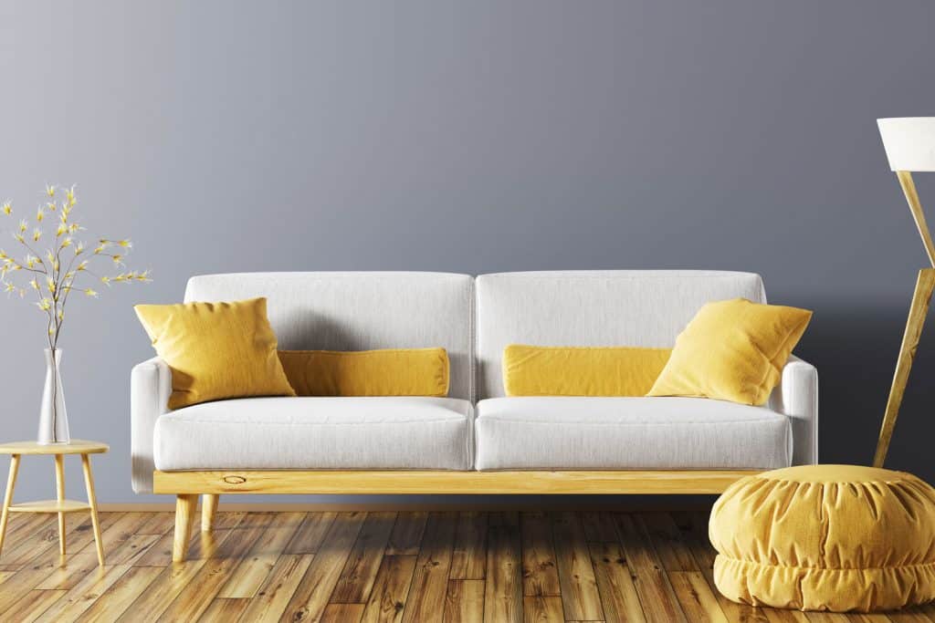 A white love seat with yellow throw pillows inside a gray themed living room