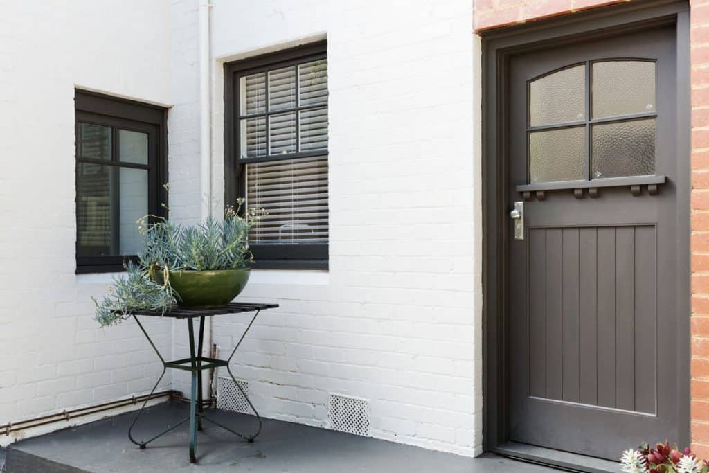A white painted front porch wall with windows and a wooden gray front door with panels