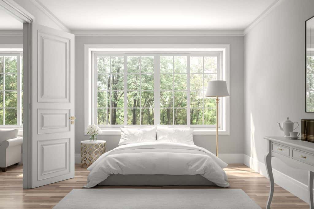 A simple white color inspired living room with white beddings, white floor lamp, and a picture window on the background