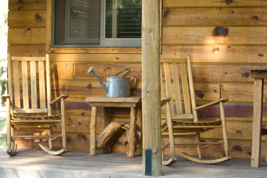 A wooden themed front porch with wooden rocking chairs and a center table with a sprinkler