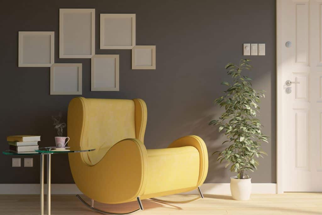 A yellow curved reading chair, glass coffee table, mock up picture frames on the gray wall