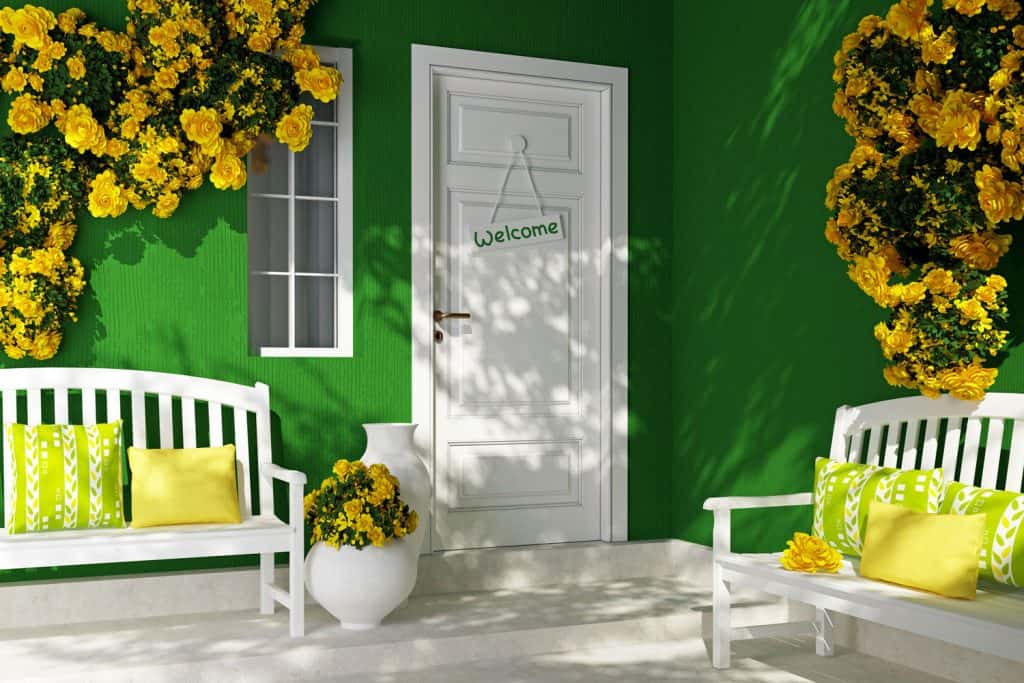 An eco themed front porch with yellow flowers on the walls, white front door, and white benches with throw pillows