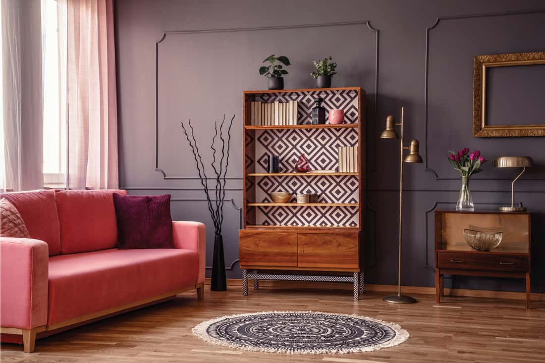 Antique wooden bookcase with decorations in an elegant gray living room interior with a comfortable powder pink sofa and boho chic round rug