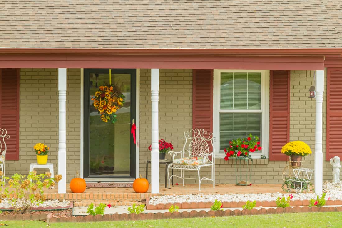 Beautiful house decorated for Halloween with pumpkins and seasonal flowers at the principal entrance in a warm autumn afternoon. Halloween / Fall Decoration Adorns Beautiful Entry Way To Home. Front Porch decorated for the Halloween, Thanksgiving, Autumn season background.