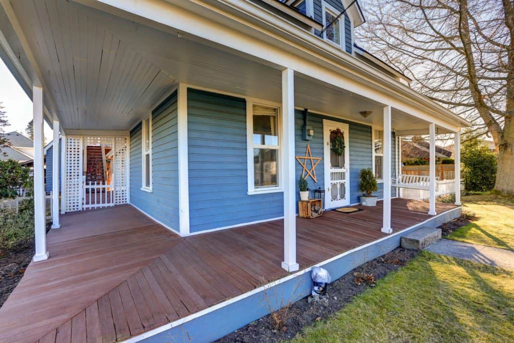 Blue wooden siding front porch with white painted columns and brown wooden flooring
