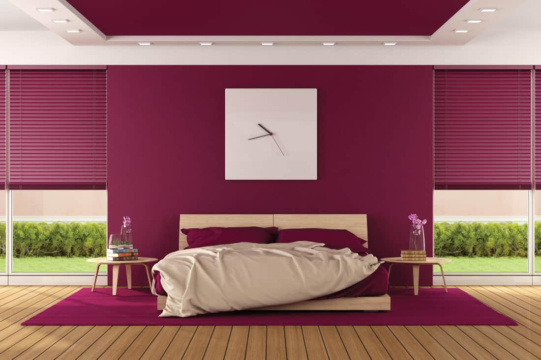 Boldly Burgundy bedroom with large white wall clock above the bed, tan floor and furnitures