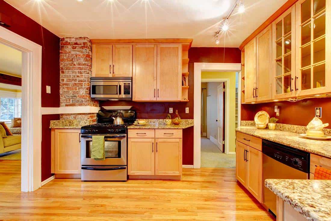 Bright kitchen room with wooden cabinets, brick designed wall and vinyl floor