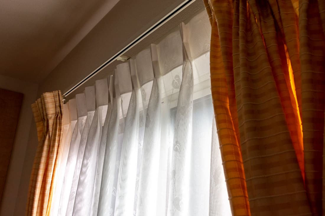 Brown and white pinch pleated curtains inside a modern living room, How To Hang Pinch Pleat Curtains [5 Steps]