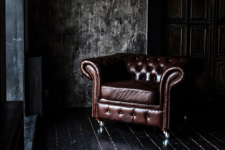 Chesterfield Sofa of brown leather standing in center on concrete floor against dark grey wall with copy space, What Goes With A Chesterfield Sofa?