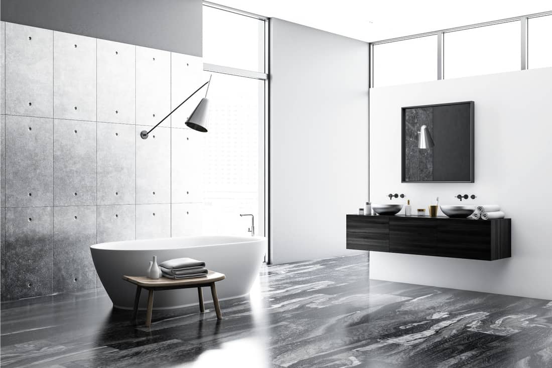 Concrete and white bathroom interior with a black marble floor, a white bathtub, a double sink and a loft window