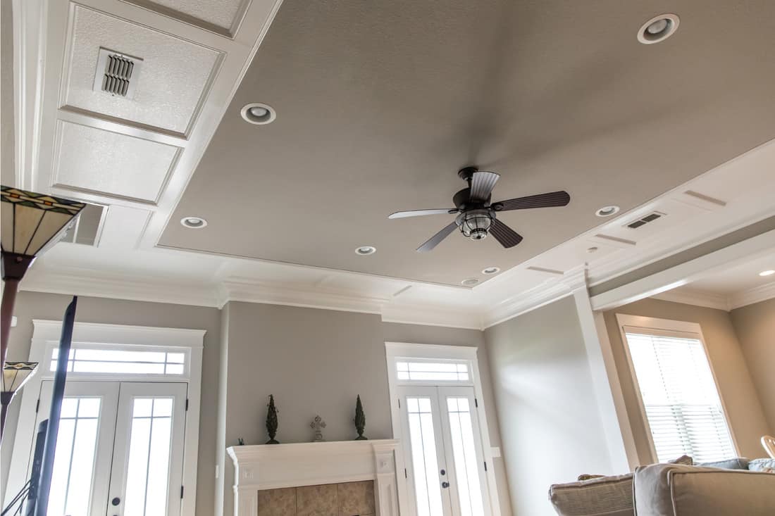 Detailed trim white wood tray ceiling with a ceiling fan in a beige greige gray new construction house. Grey Ceiling, White Trim, And Grey Walls
